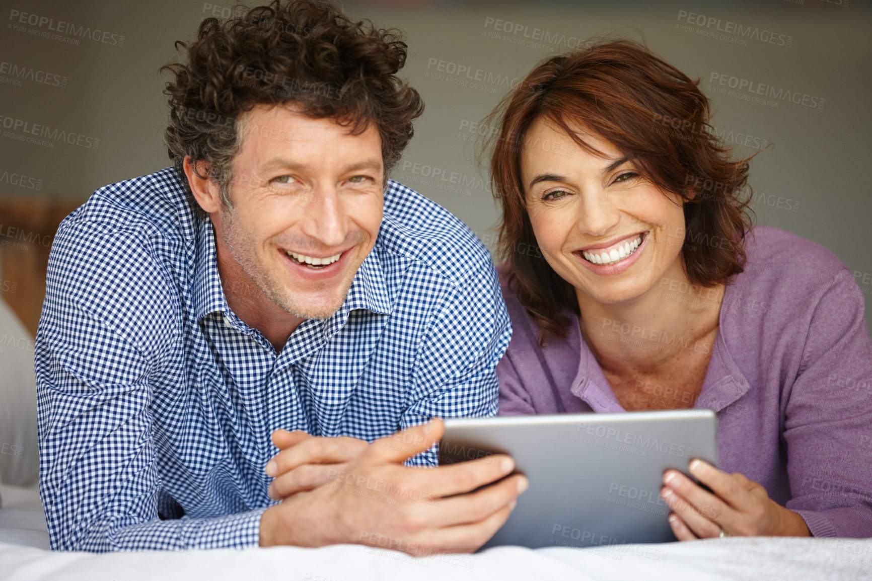 Buy stock photo Shot of a couple using a digital tablet while lying on bed