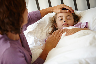 Buy stock photo Shot of a caring mother feeling the forehead of her sick little girl