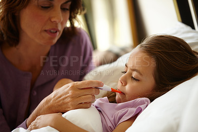 Buy stock photo Shot of a little girl lying in bed while her mother takes her temperature with a thermometer