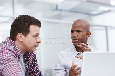 Buy stock photo A young designer trying to explain something to his colleague as they sit by a desk with a laptop