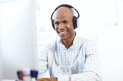 Buy stock photo Shot of a happy-looking african american designer at work on a desktop computer in the office and wearing a headphones