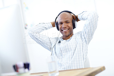 Buy stock photo Portrait of a relaxed-looking african american designer leaning back in his chair in front of a desktop computer in the office and wearing a headphones