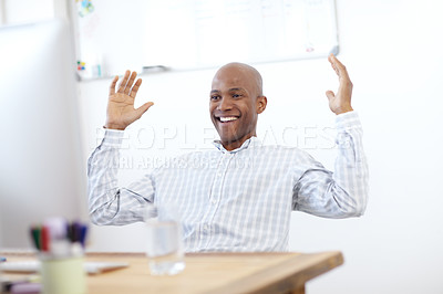 Buy stock photo Shot of an excited-looking african american designer leaning back in his chair in front of a desktop computer in the office and raising his arms in celebration