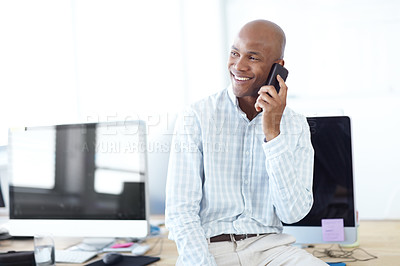 Buy stock photo Shot of a young businessman talking on the phone while sitting on a desk lined with computers