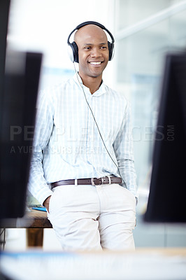 Buy stock photo Shot of a young businessman wearing headphones standing between monitors in the foreground