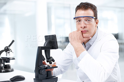 Buy stock photo A serious scientist sitting in front of his microscope while looking at the camera