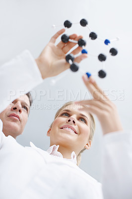 Buy stock photo Low angle shot of two young scientists looking at a molecular structure model