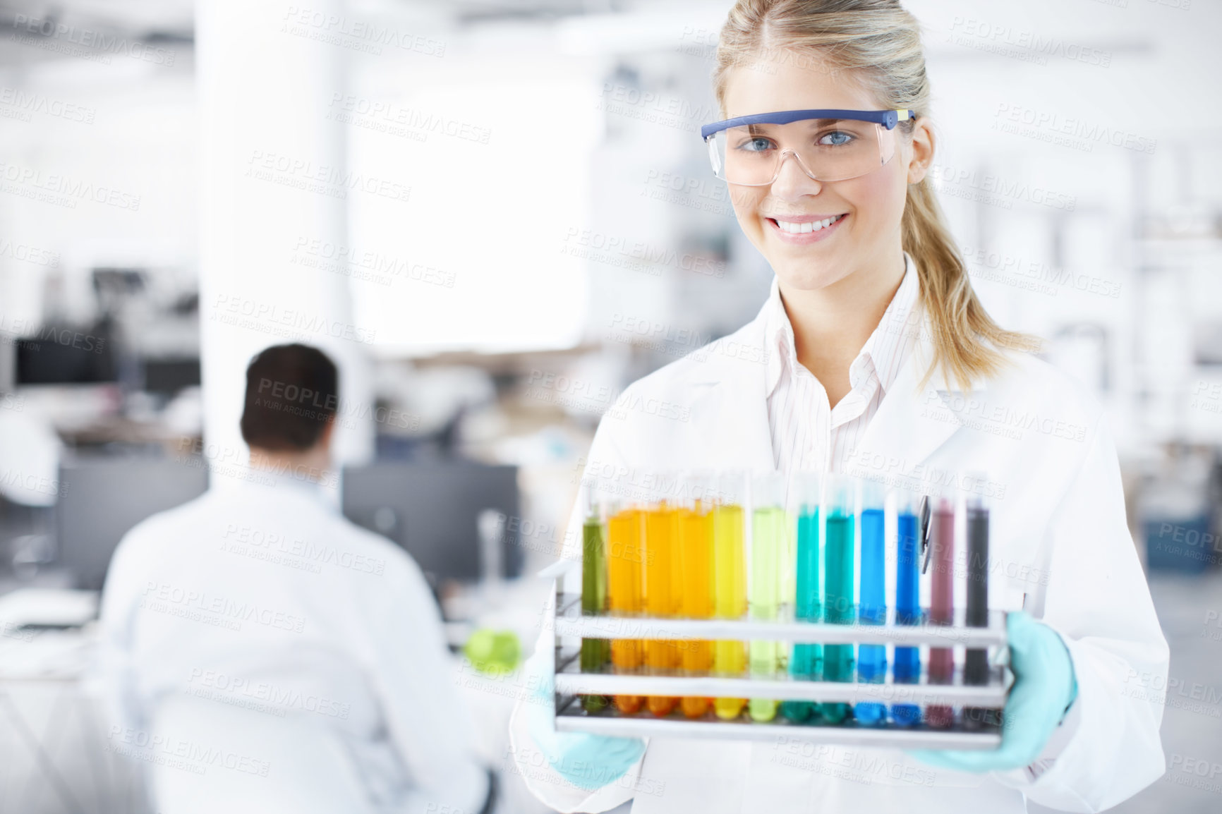 Buy stock photo Portrait of a beautiful young scientist carrying a tray of test tubes with a male colleague in the background