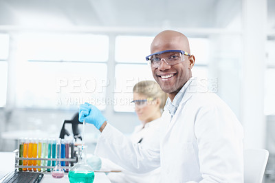 Buy stock photo Portrait of a smiling young chemist working in the lab with a female coworker in the background