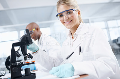 Buy stock photo Portrait of a gorgeous female scientist in front of a microscope with a male colleague in the background