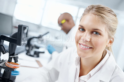 Buy stock photo Closeup portrait of a gorgeous female scientist in front of a microscope with a male colleague in the background