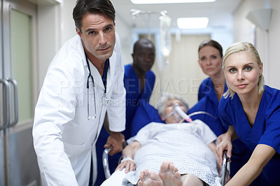 Buy stock photo Portrait of a group of doctors pushing a patient down the hall