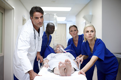 Buy stock photo A group of doctors pushing a patient down the hall