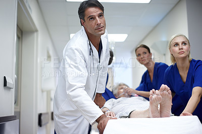 Buy stock photo A team of doctors pushing a patient down the hall