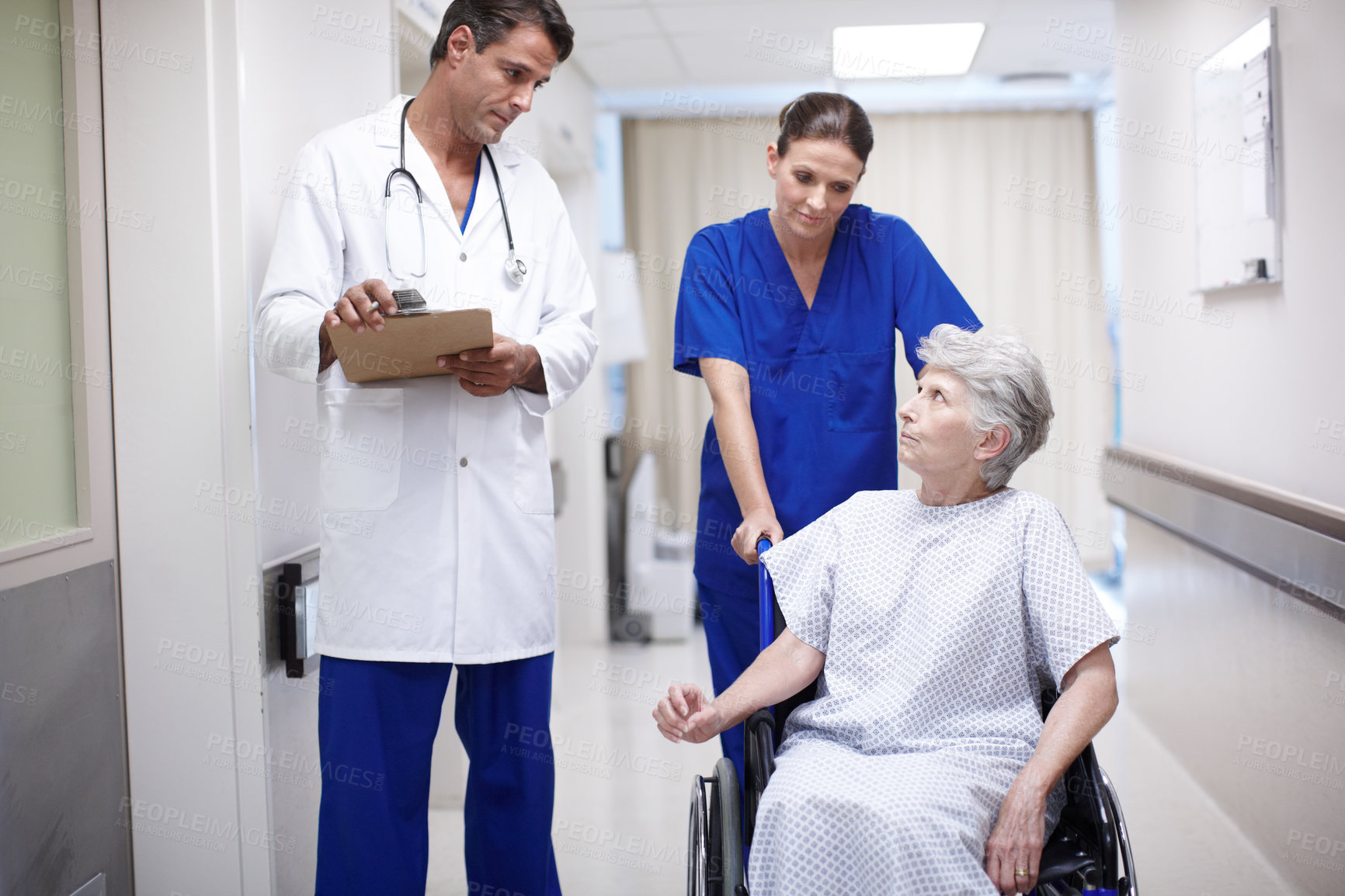 Buy stock photo A female nurse pushing a senior patient in a wheelchair down the hall while she talks with her doctor