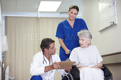 Buy stock photo A female nurse pushing a senior patient in a wheelchair down the hall while talking with her doctor
