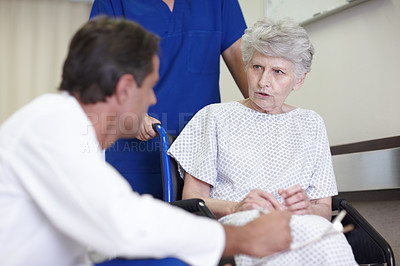 Buy stock photo A female nurse pushing a senior patient in a wheelchair down the passage while talking with her doctor