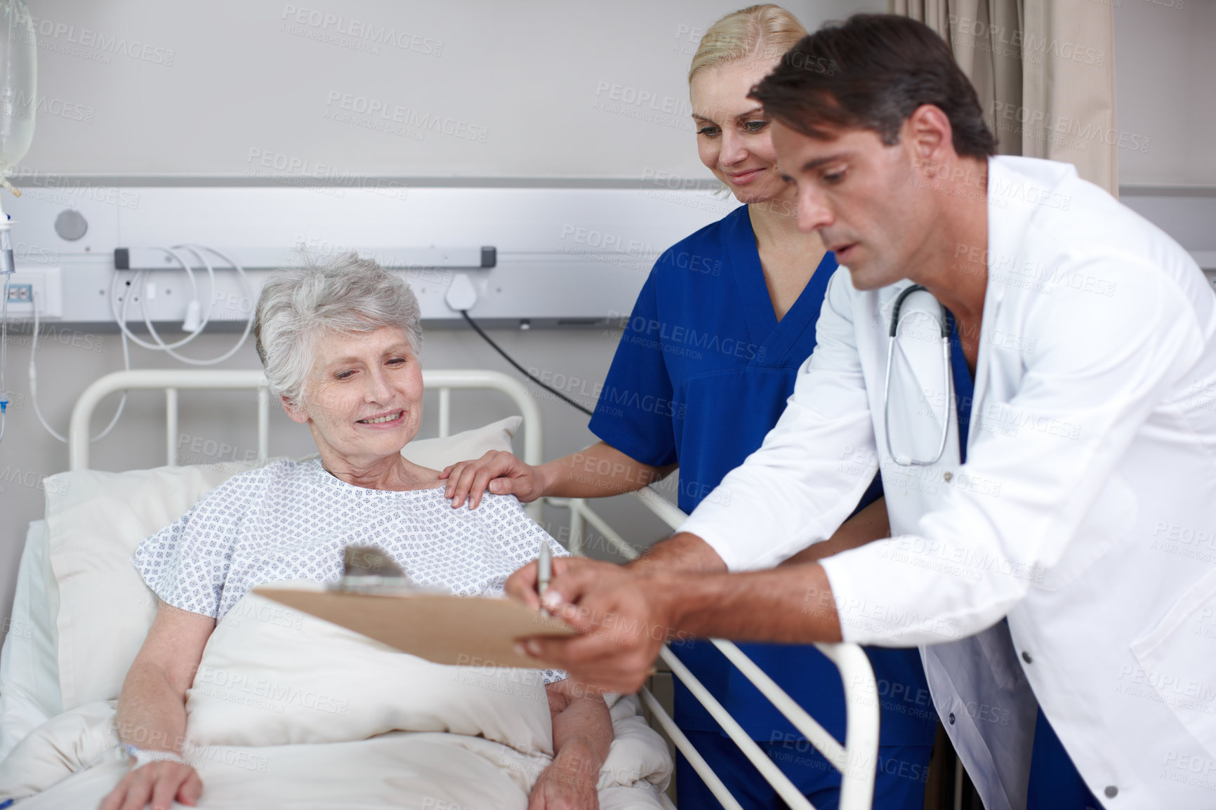 Buy stock photo A doctor and his young nurse showing her where to sign the medical report while standing over her bed