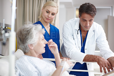 Buy stock photo A doctor and his young nurse talking with their patient her medical report while standing over her bed