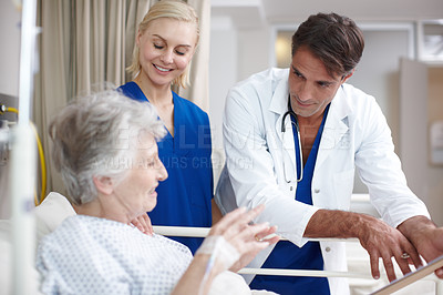 Buy stock photo A doctor and his young nurse discussing options with their patient while holding her medical report while standing over her bed