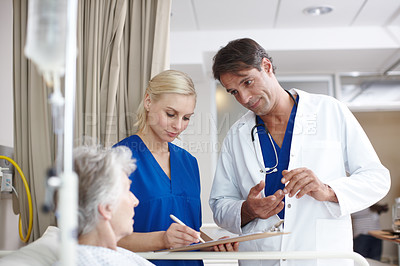 Buy stock photo A doctor and his young nurse filling their patient's medical report while standing over her bed