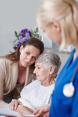 Buy stock photo A daughter consoling her mother in the clinic as a young nurse looks on