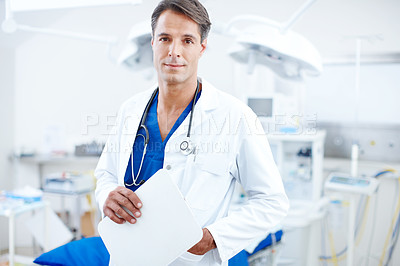 Buy stock photo A confident male doctor standing in the operating theatre holding a chart