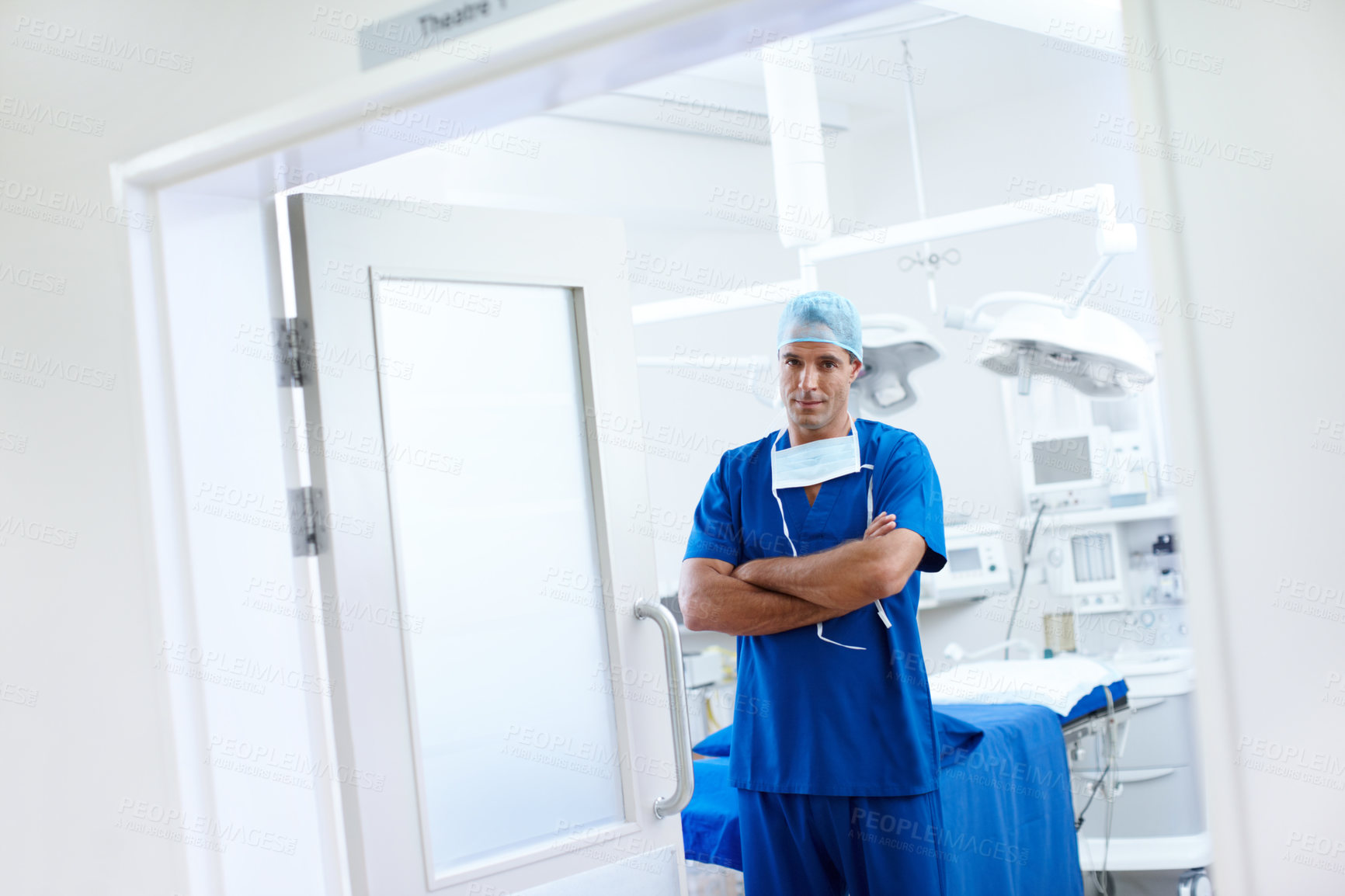 Buy stock photo A handsome male doctor standing in the doorway of his operating theatre