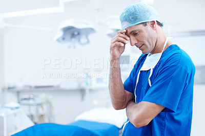 Buy stock photo A worried looking doctor standing with his hand on his head looking down