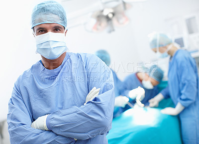 Buy stock photo Portrait of a confident surgeon standing in an operating theatre with his team in the background