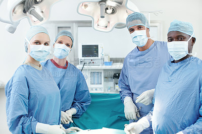 Buy stock photo Portrait of a diverse group of surgeons wearing hospital scrubs and face masks in an operating theatre
