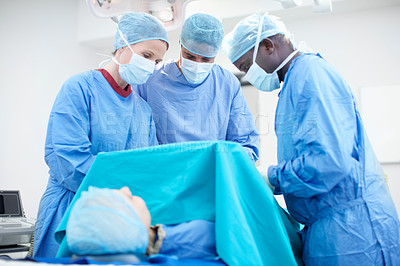 Buy stock photo Diverse group of surgeons working together on a patient wearing scrubs in an operating room