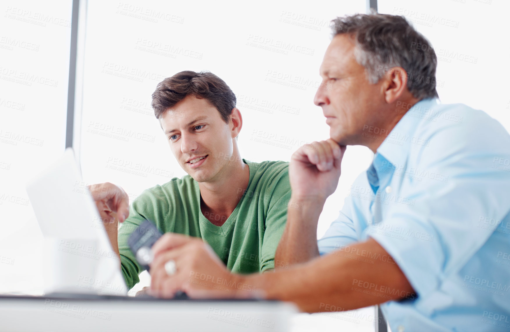 Buy stock photo A mature executive looking over some work on a laptop with a younger colleague