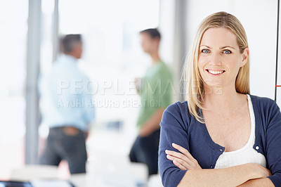 Buy stock photo Portrait of a young woman standing with her arms folded and her colleagues behind her