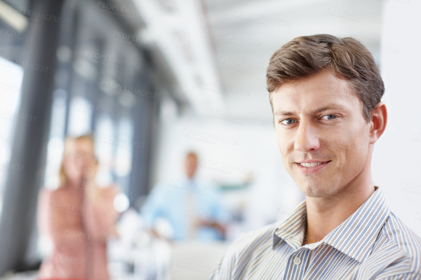 Buy stock photo Portrait of a young designer sitting at his desk with colleagues in the background