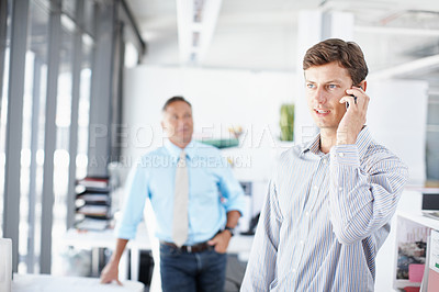 Buy stock photo A young professional talking on his cellphone as a colleague stands in the background