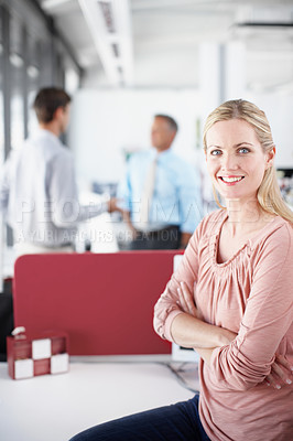 Buy stock photo Portrait of a young businesswoman crossing her arms as colleagues converse in the background