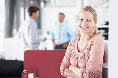 Buy stock photo Portrait of a young businesswoman crossing her arms as colleagues converse in the background