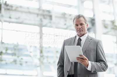 Buy stock photo Portrait of a mature businessman using a digital tablet while standing in the office