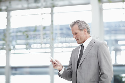 Buy stock photo Mature businessman texting on his cellphone while standing in the office