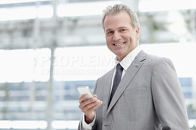 Buy stock photo Portrait of a mature businessman texting on his cellphone while standing in the office