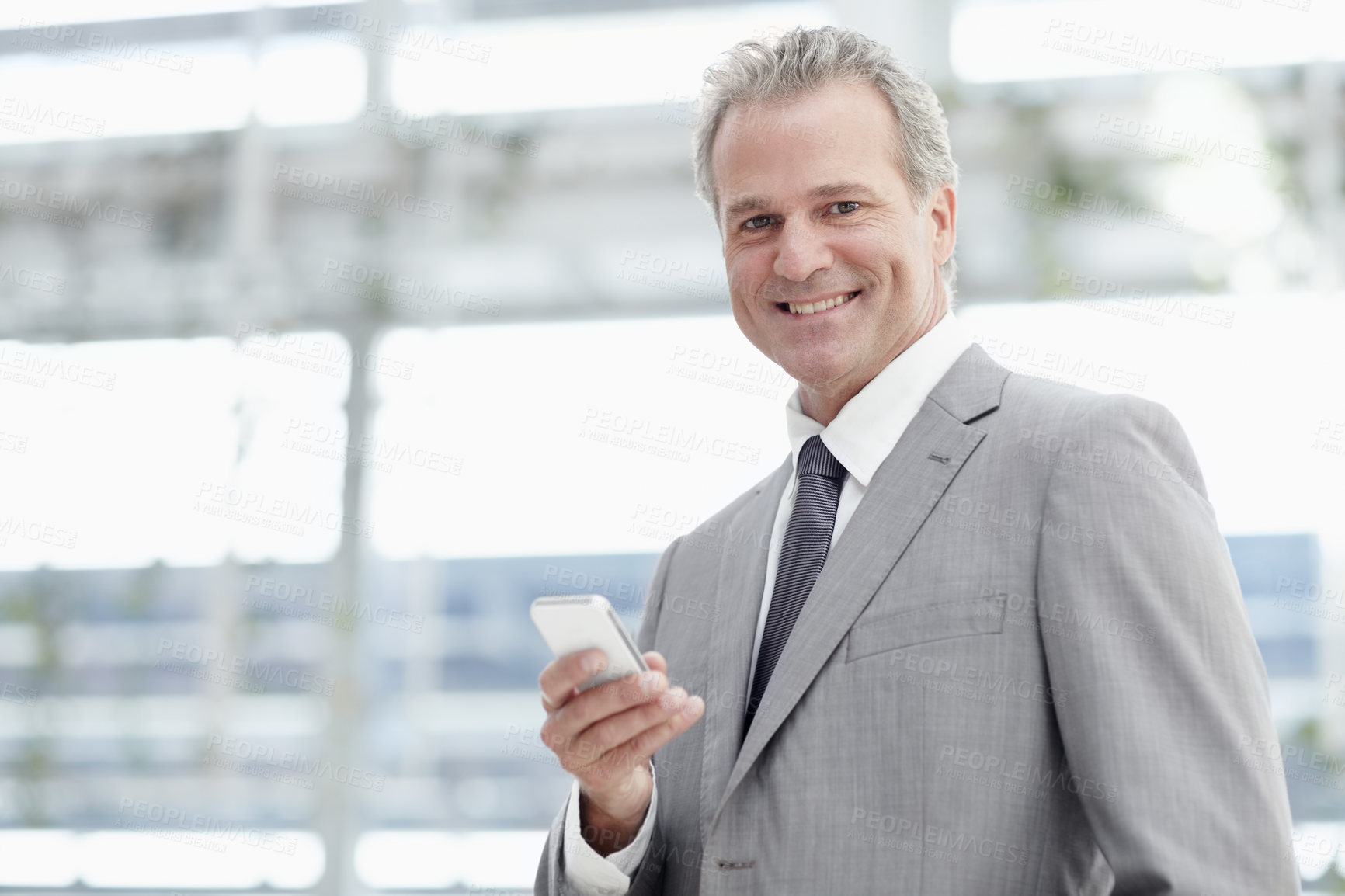 Buy stock photo Portrait of a mature businessman texting on his cellphone while standing in the office