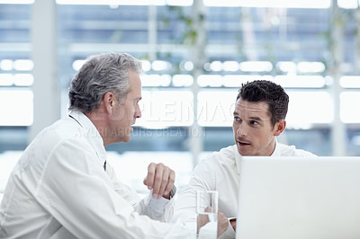 Buy stock photo Two businessmen talking while sitting in front of a laptop