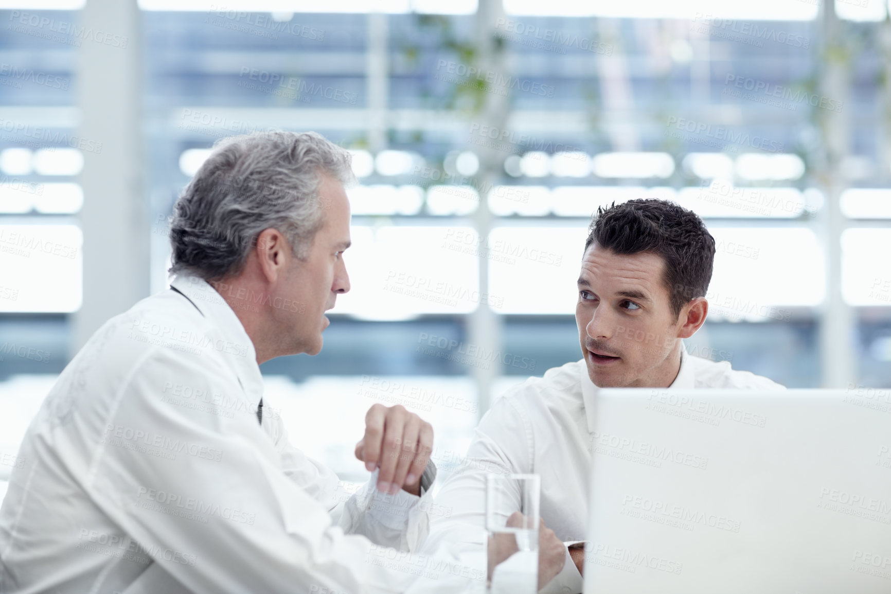 Buy stock photo Two businessmen talking while sitting in front of a laptop