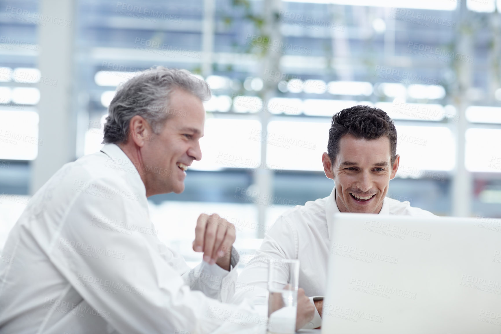 Buy stock photo Two businessmen talking while sitting in front of a notebook