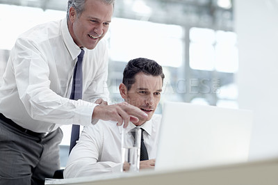 Buy stock photo A mature businessman pointing to a laptop while standing behind a younger colleague