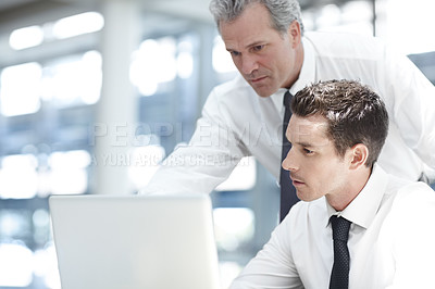 Buy stock photo A mature businessman standing behind a younger colleague while viewing a laptop