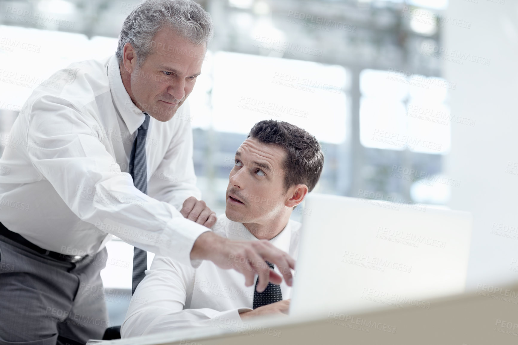 Buy stock photo A mature businessman pointing to a notebook while standing behind a younger colleague