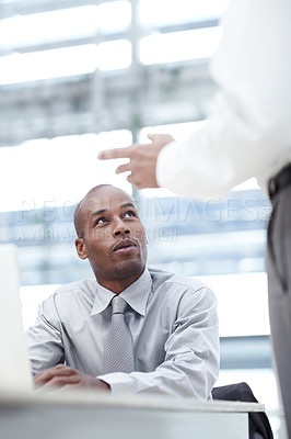 Buy stock photo A businessman sitting down in front of his laptop and looking up to a colleague as they discuss business
