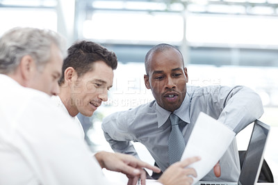 Buy stock photo Three businessmen looking over documents while sitting down in a meeting